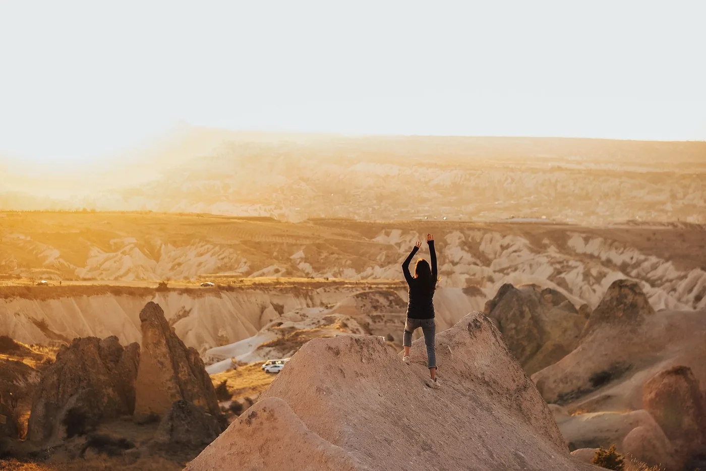 Mulher no topo de uma montanha, de braços erguidos ao nascer do sol