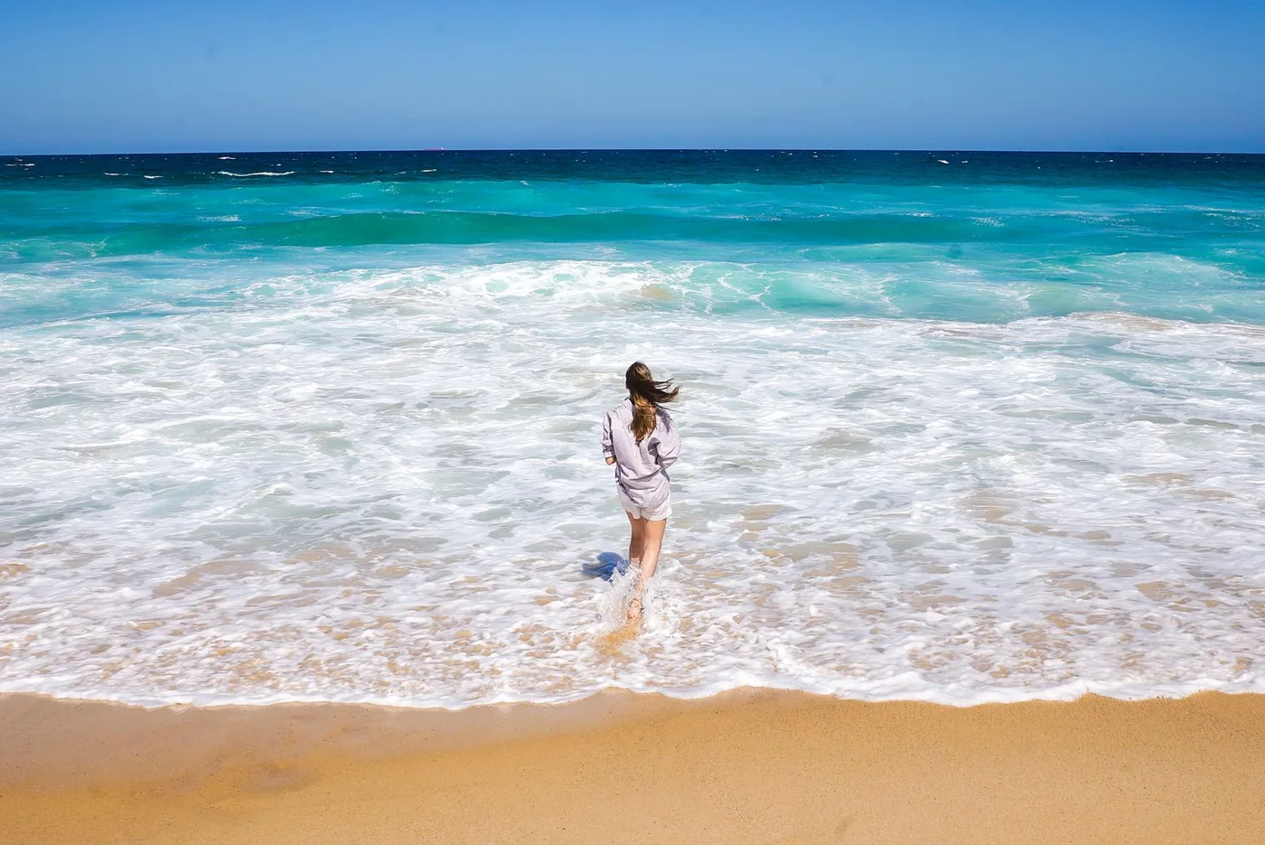 Mulher caminhando em direção ao mar, olhando para o horizonte